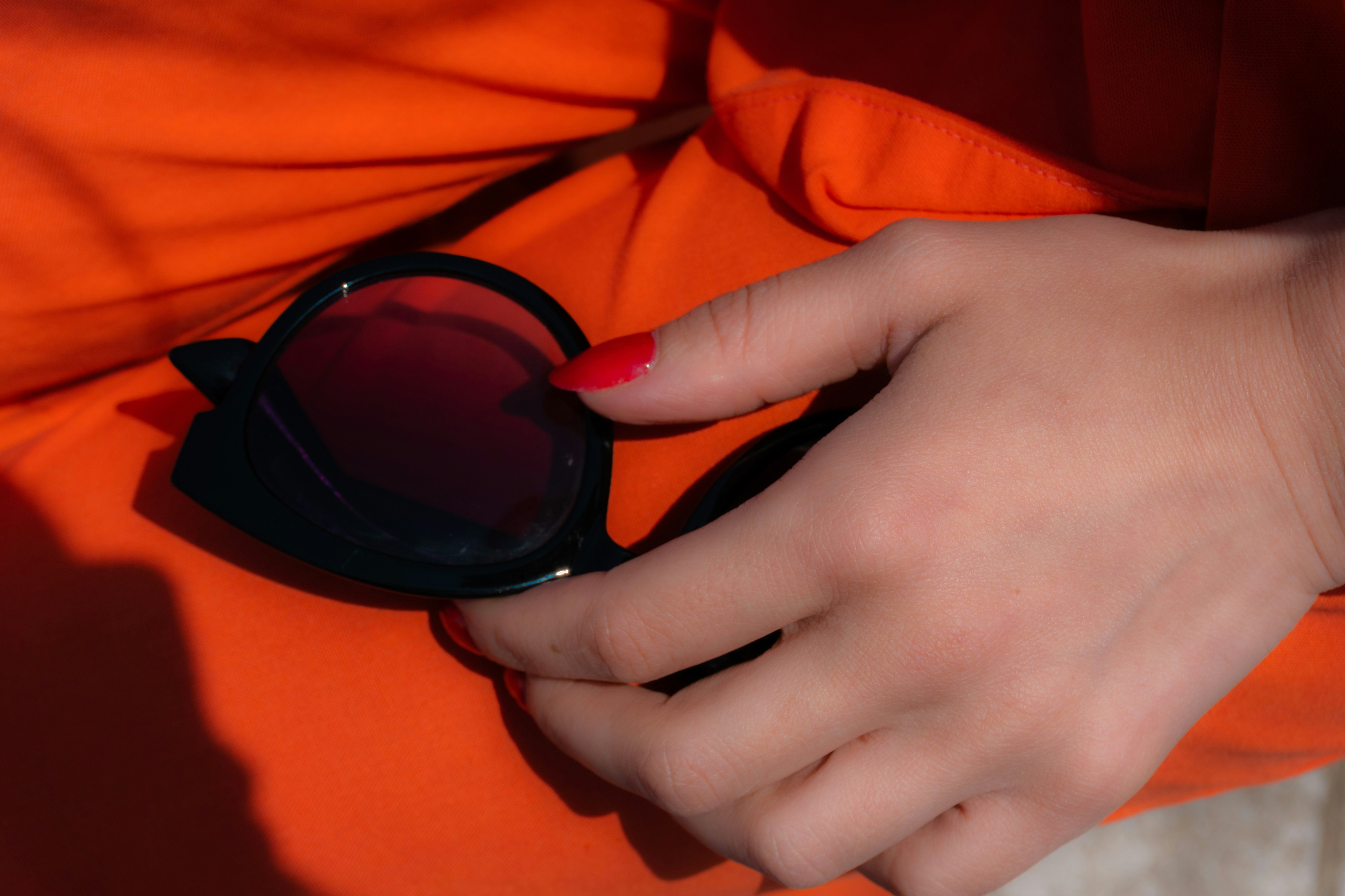 Hand with coral nails holding sunglasses against a warm orange dress